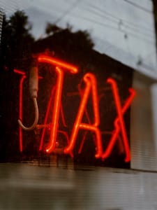 Understanding the 2025 Federal Estate Tax Threshold Increase A close-up, slightly blurry view of a bright red neon sign that reads 'TAX' mounted on a dark, reflective surface.
