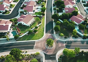Navigating California Property Tax Reassessment Risks for Inherited Homes An aerial view of a quiet suburban neighborhood in California featuring single-family homes with red tile roofs, swimming pools, and a central roundabout intersection with a tree in the middle.